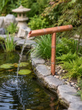 Copper tee spout pouring water into a Japanese style garden pond